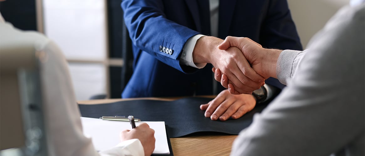 Broker shaking hands across a desk with a client.