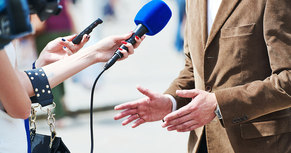 Female reporter with microphone interviews male in sport jacket.